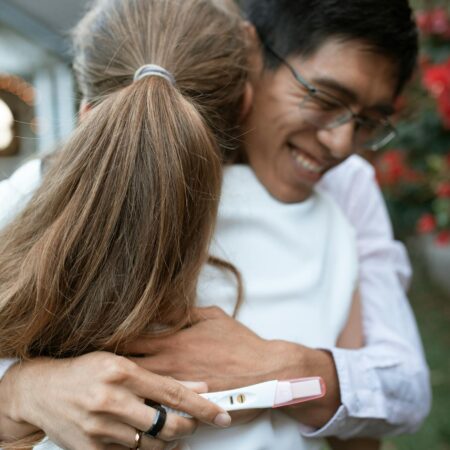 A couple shares a joyful hug outdoors, celebrating a positive pregnancy test result.