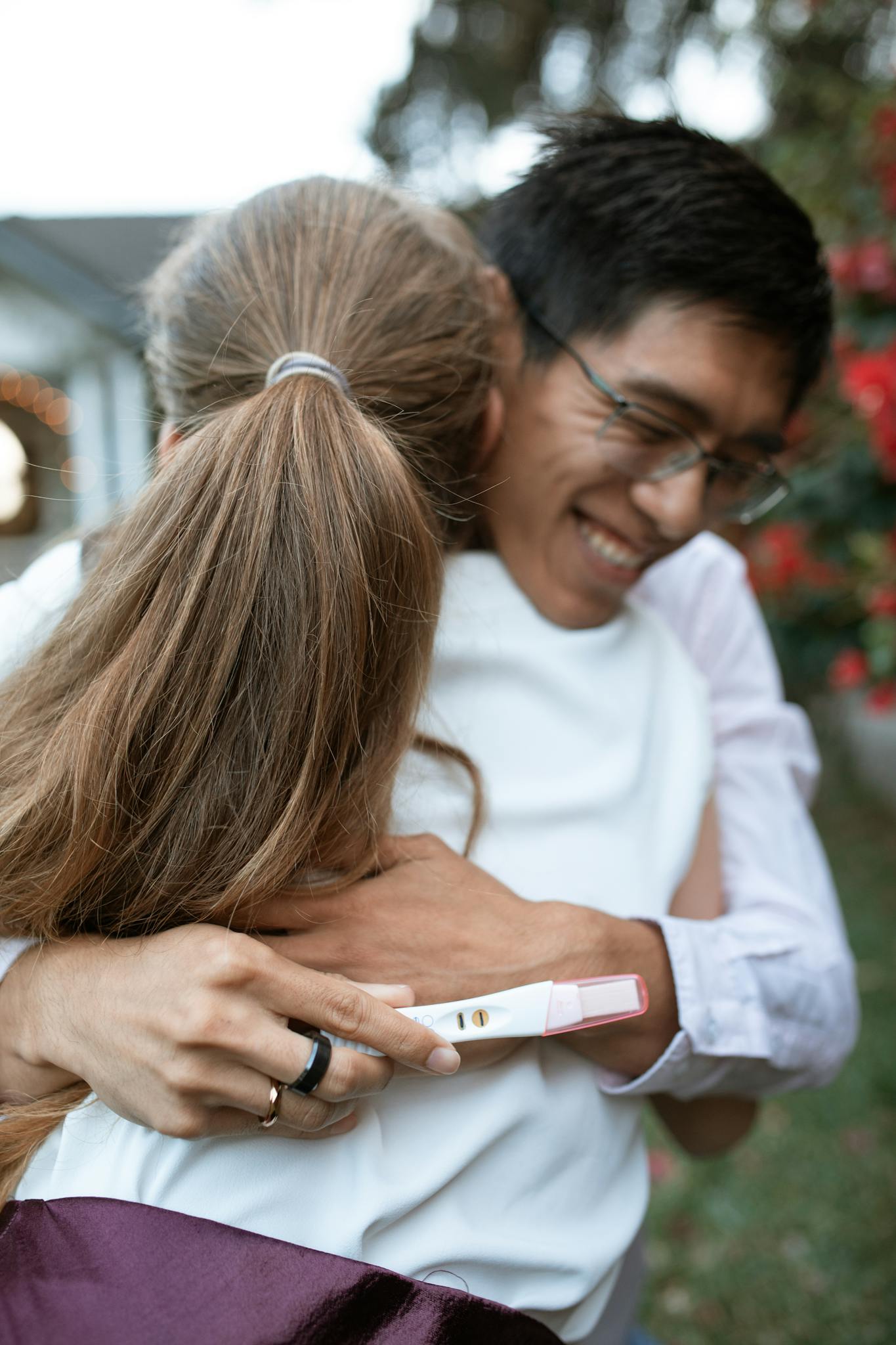 A couple shares a joyful hug outdoors, celebrating a positive pregnancy test result.