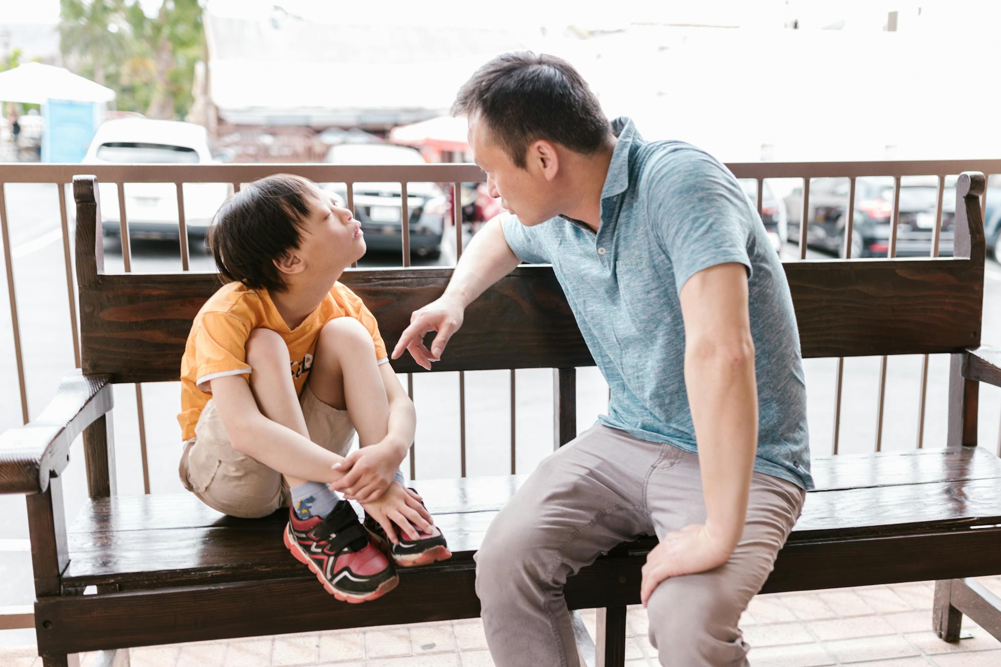 A heartfelt interaction between father and son sitting on a wooden bench outdoors, promoting bonds and autism awareness.